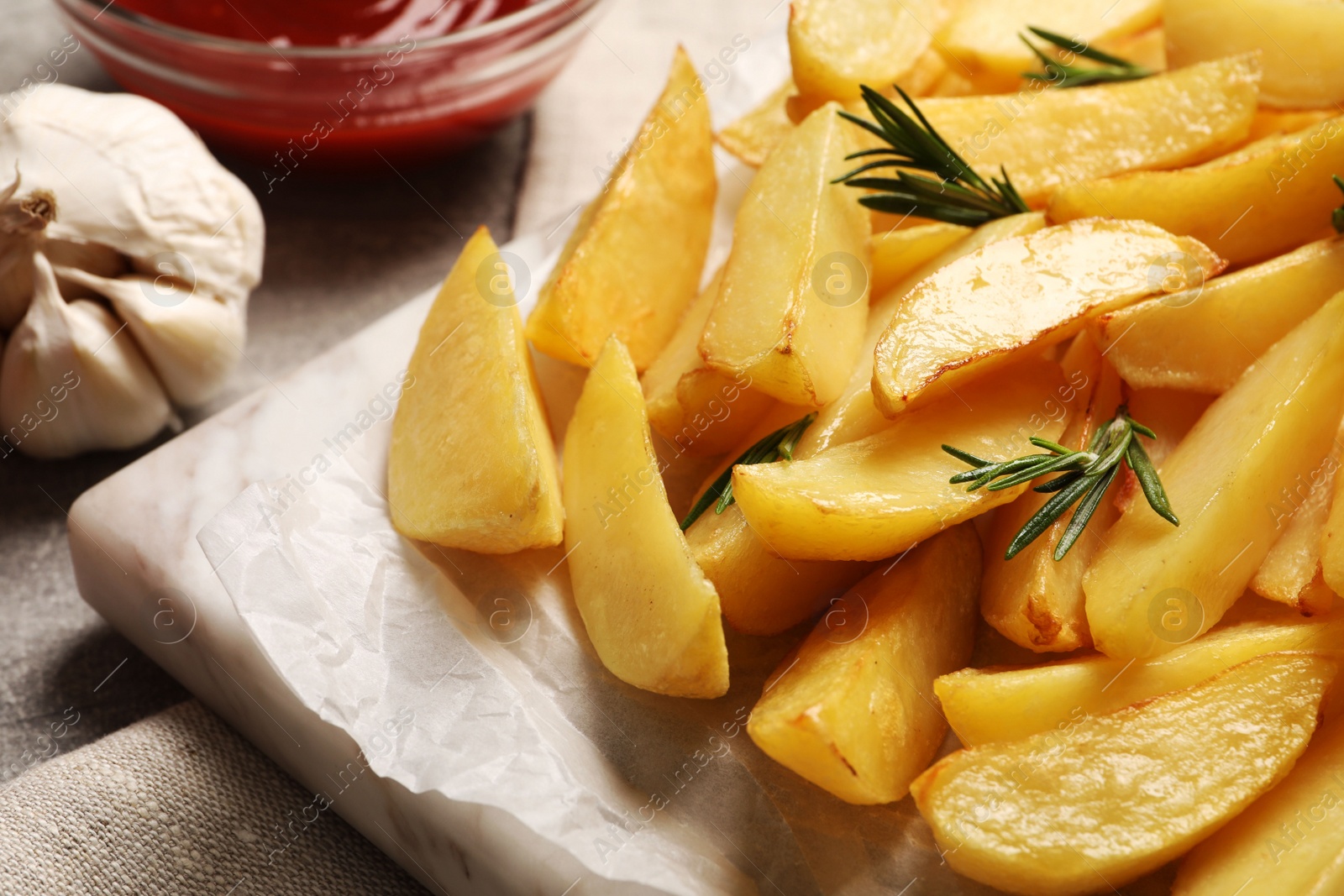 Photo of Tasty baked potato wedges, garlic and rosemary on table, closeup