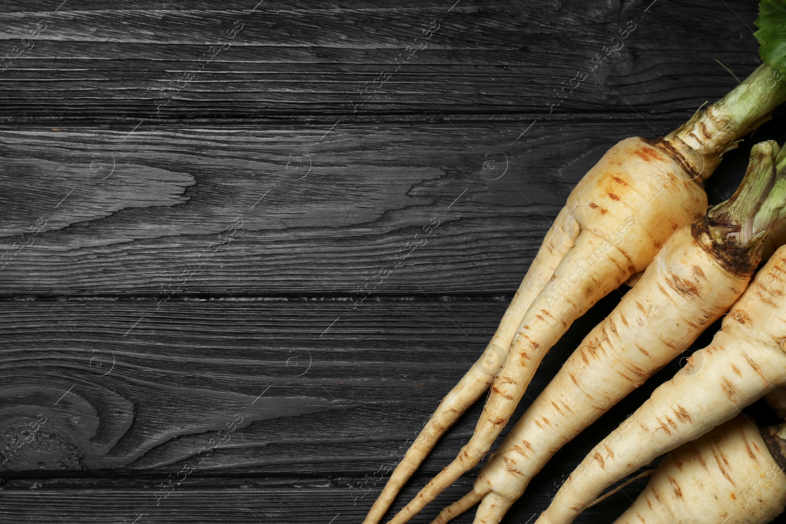 Photo of Tasty fresh ripe parsnips on black wooden table, flat lay. Space for text
