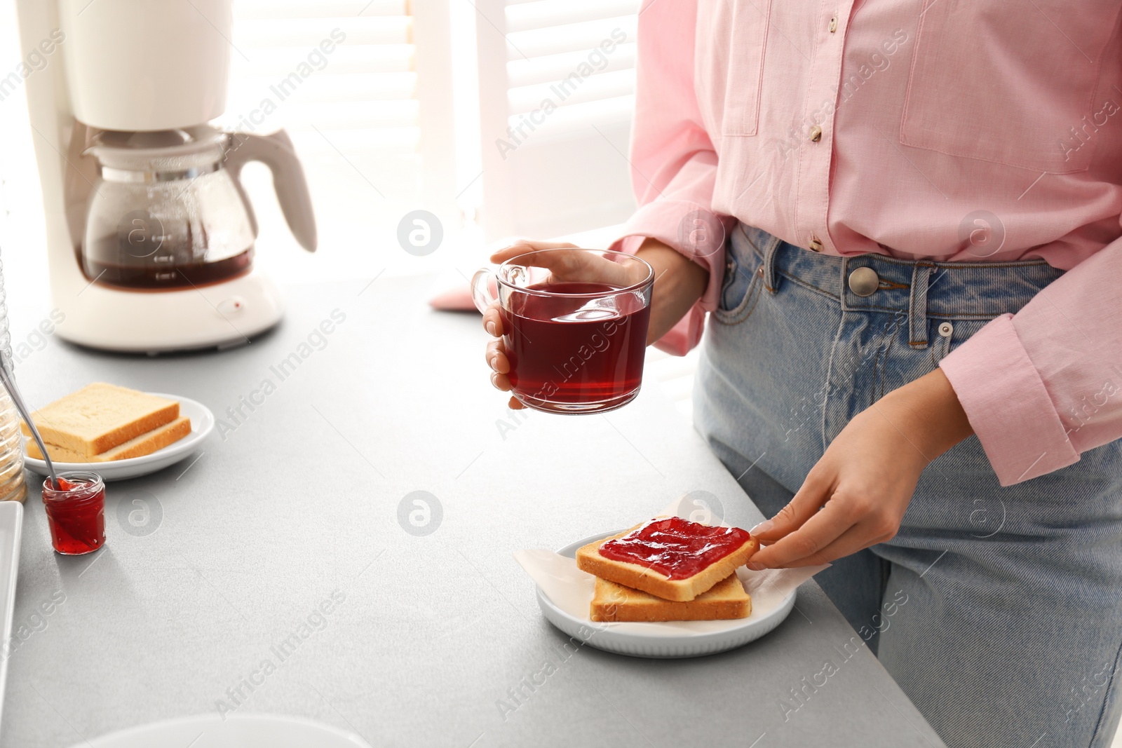 Photo of Woman having tasty breakfast with toast and raspberry tea at home, closeup. Morning routine