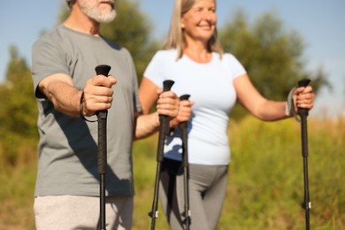 Photo of Senior couple practicing Nordic walking with poles outdoors on sunny day, selective focus