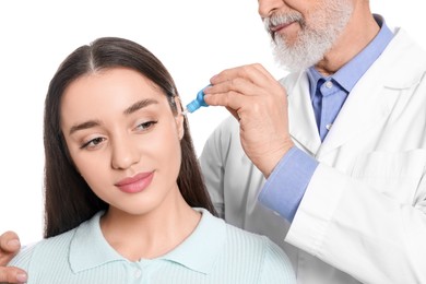 Doctor dripping medication into woman's ear on white background