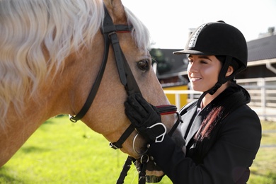 Young woman in horse riding suit and her beautiful pet outdoors on sunny day