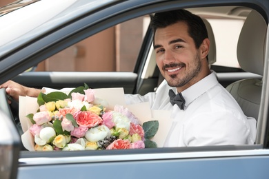 Young handsome man with beautiful flower bouquet sitting in car