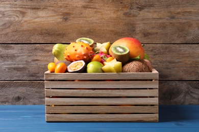 Photo of Crate with different exotic fruits on blue wooden table