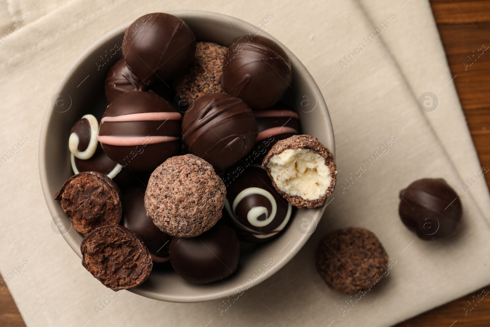 Photo of Bowl with many different delicious chocolate truffles on wooden table, top view