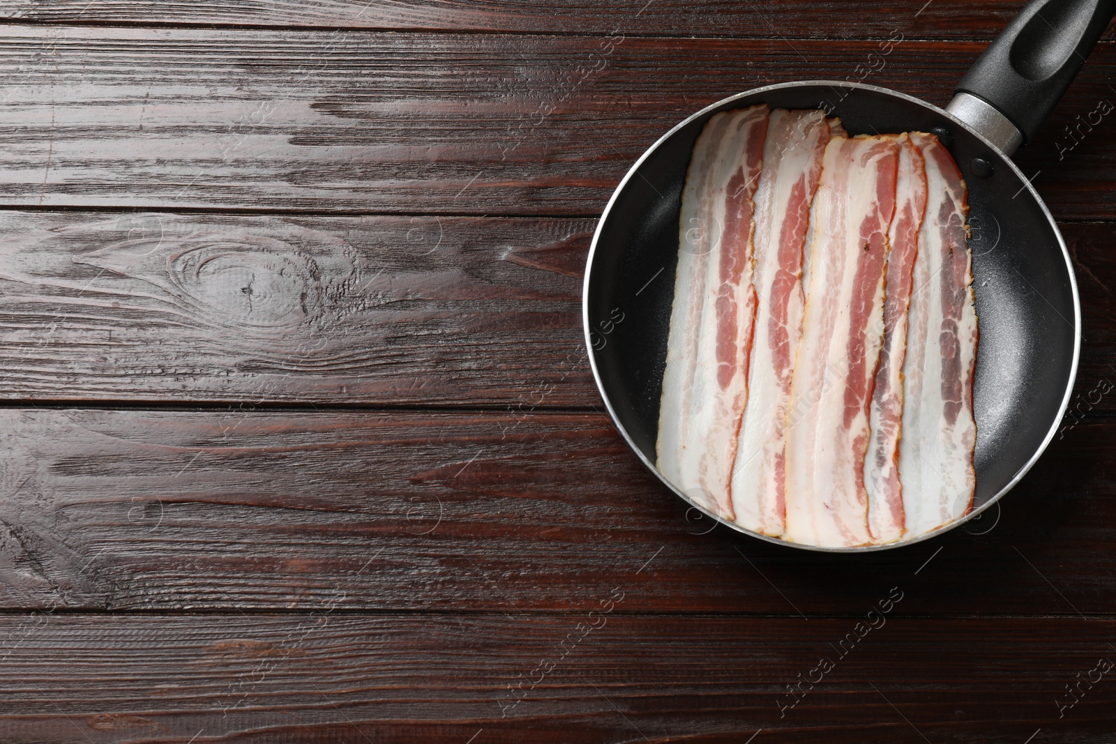 Photo of Slices of raw bacon in frying pan on wooden table, top view. Space for text