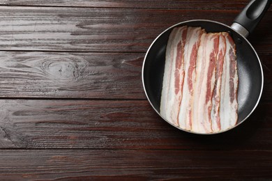 Slices of raw bacon in frying pan on wooden table, top view. Space for text