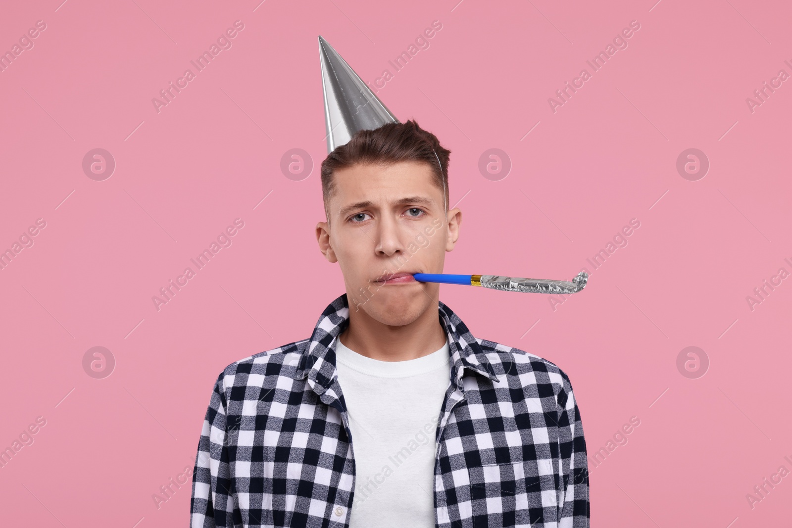 Photo of Young man in party hat with blower on pink background