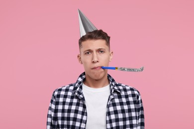 Young man in party hat with blower on pink background