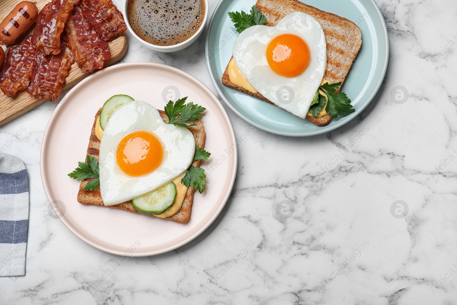 Photo of Tasty sandwiches with heart shaped fried eggs for romantic breakfast on white marble table, flat lay