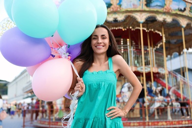 Attractive young woman with color balloons near carousel