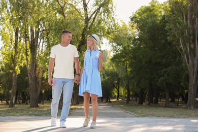 Happy couple with drink walking along park on summer day