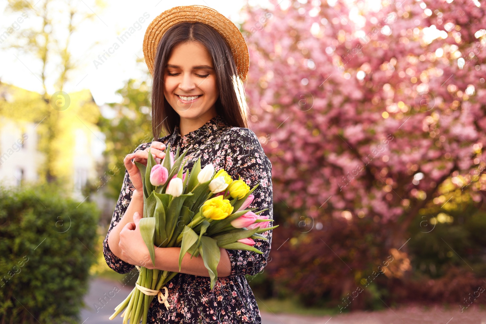 Photo of Beautiful young woman with bouquet of tulips in park on sunny day, space for text