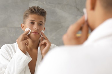 Handsome young man with cotton pads near mirror in bathroom