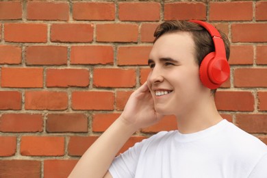 Photo of Handsome young man with headphones near red brick wall. Space for text
