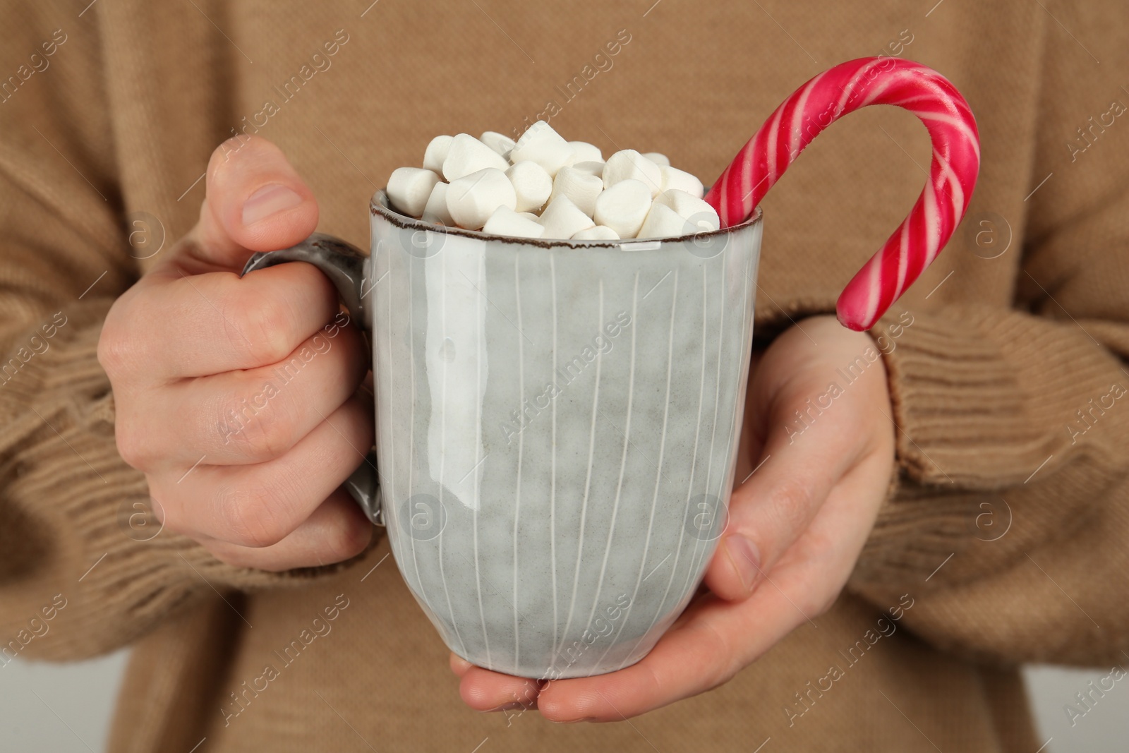 Photo of Woman holding cup of delicious hot chocolate with marshmallows and candy cane, closeup