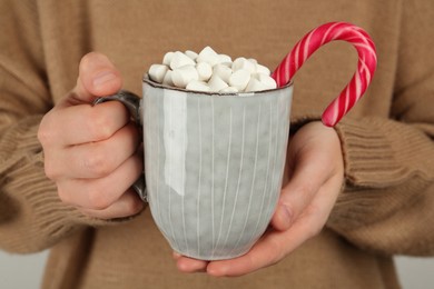 Photo of Woman holding cup of delicious hot chocolate with marshmallows and candy cane, closeup