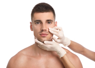 Doctor examining man's face for cosmetic surgery on white background