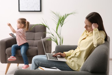 Photo of Mother working remotely on laptop while her daughter playing with smartphone at home
