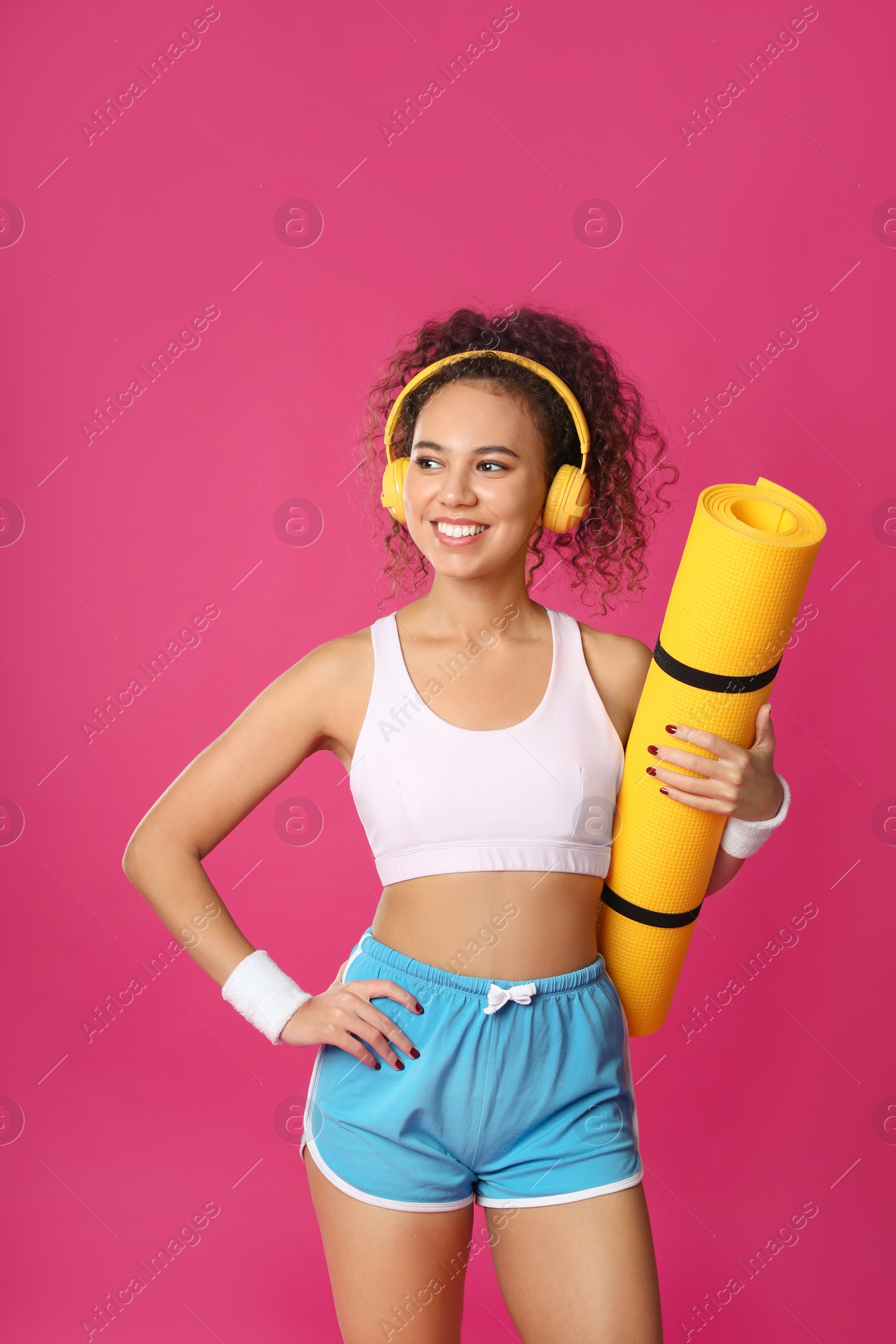 Photo of Beautiful African American woman with yoga mat and headphones on pink background