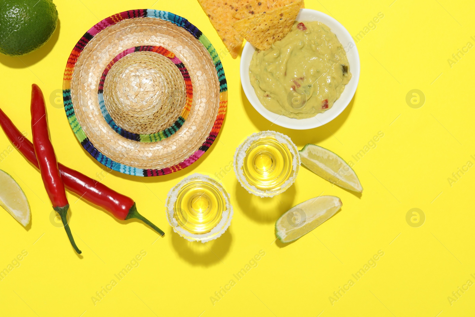 Photo of Mexican sombrero hat, tequila, nachos chips, guacamole and other products on yellow background, flat lay