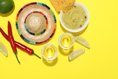 Mexican sombrero hat, tequila, nachos chips, guacamole and other products on yellow background, flat lay