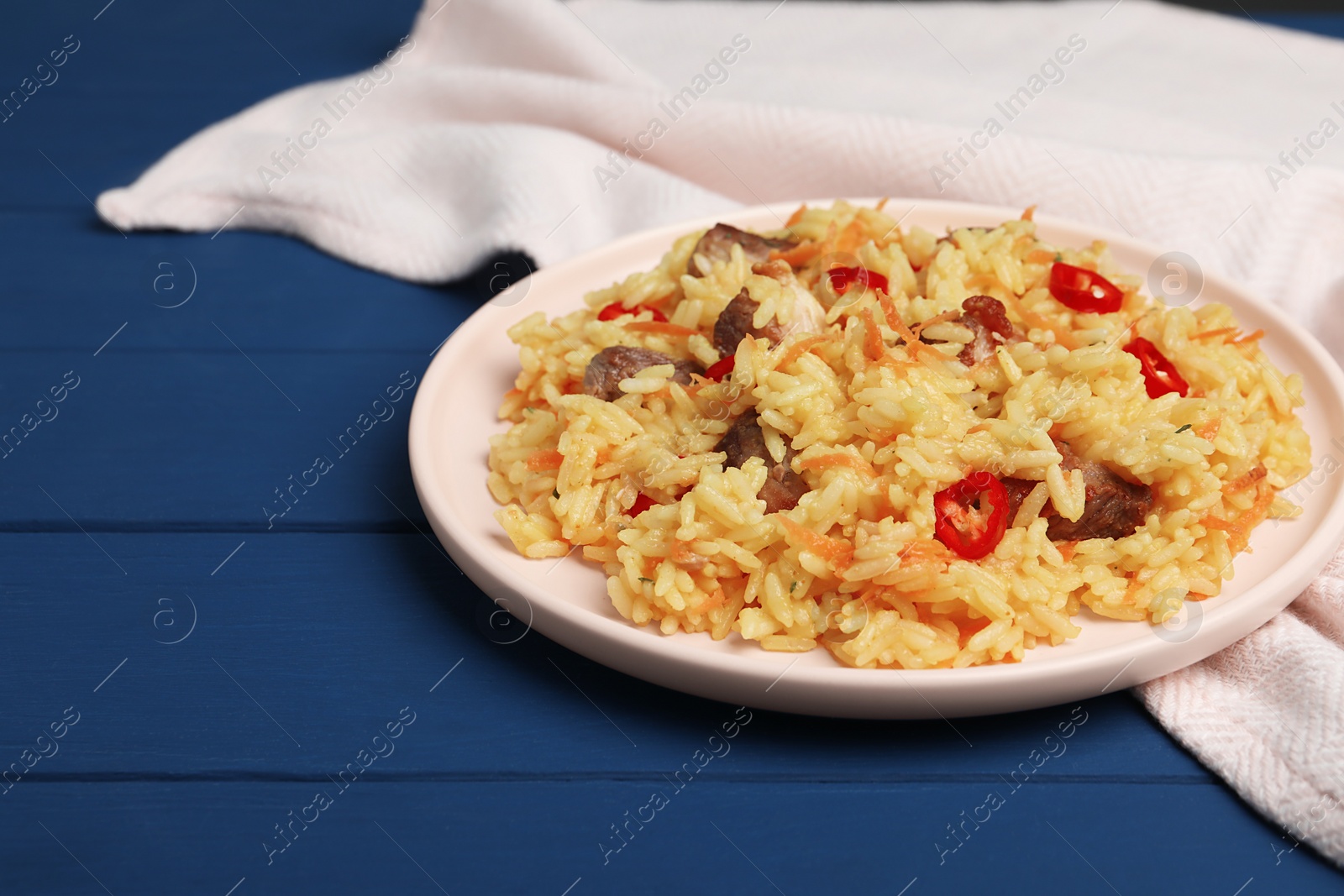 Photo of Delicious pilaf with meat on blue wooden table. Space for text