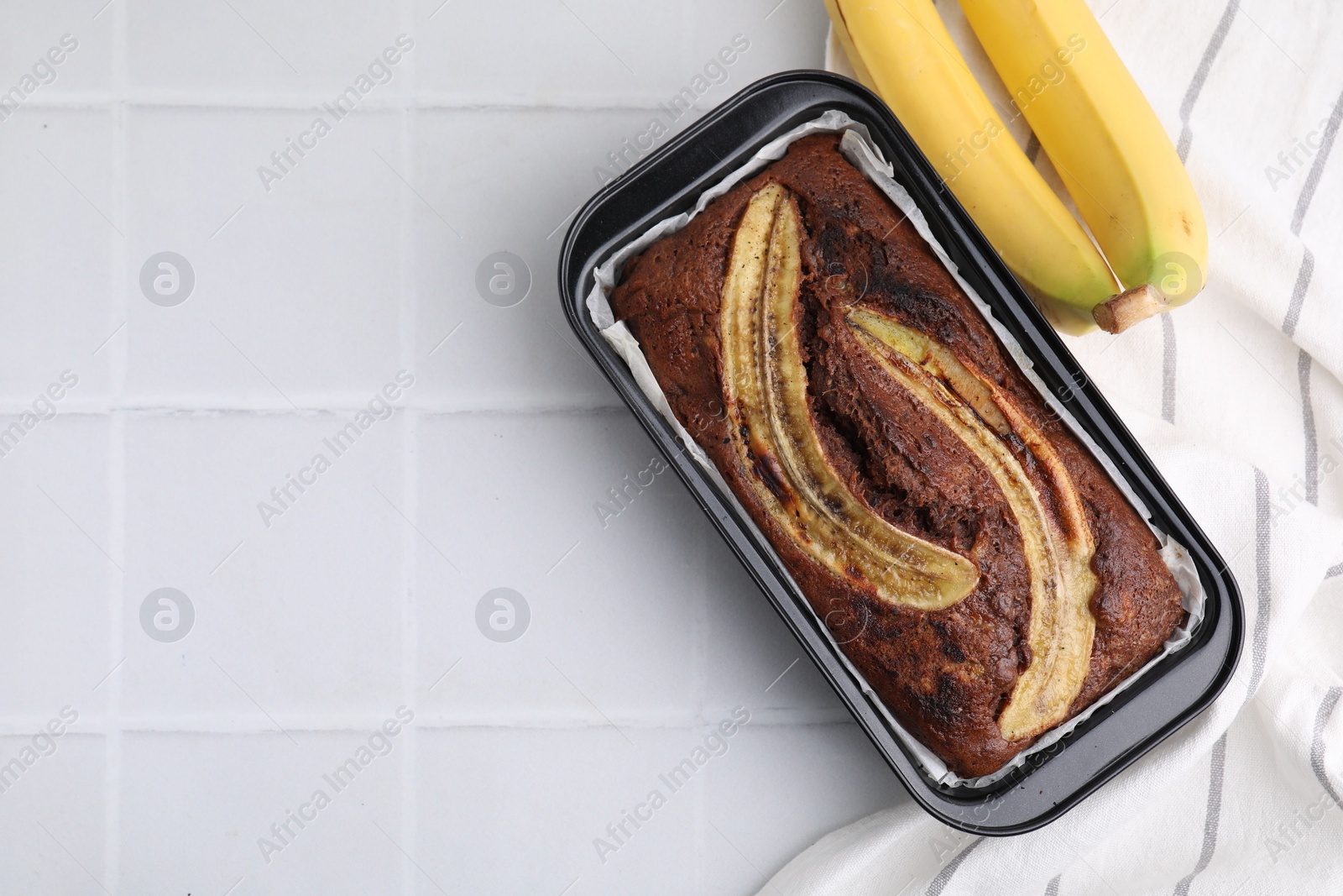 Photo of Delicious banana bread and fresh fruits on white tiled table, top view. Space for text