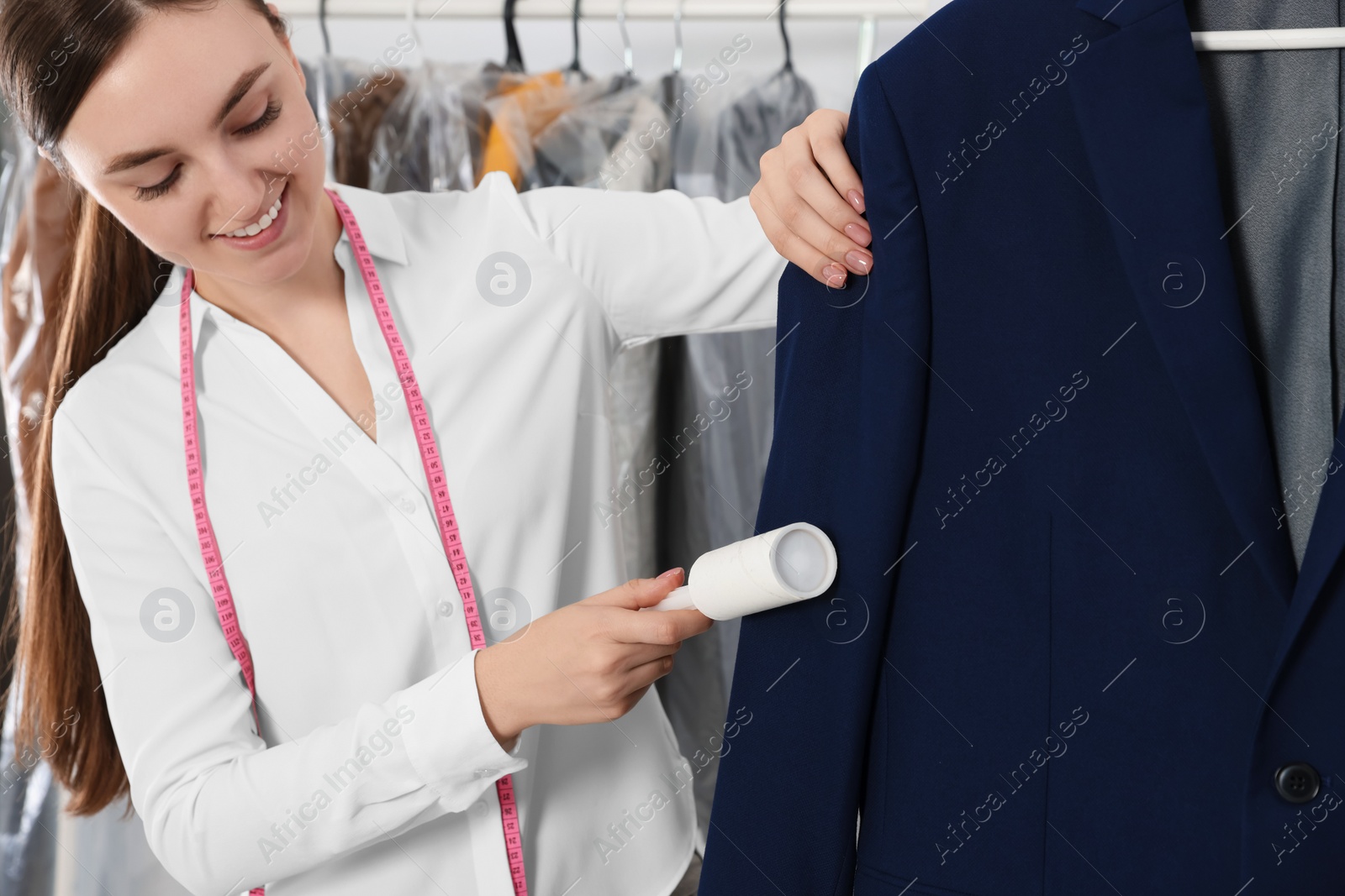 Photo of Young woman using adhesive lint roller at dry-cleaner's