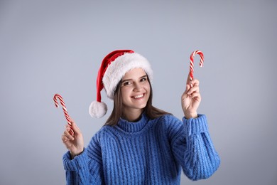 Pretty woman in Santa hat and blue sweater holding candy canes on grey background