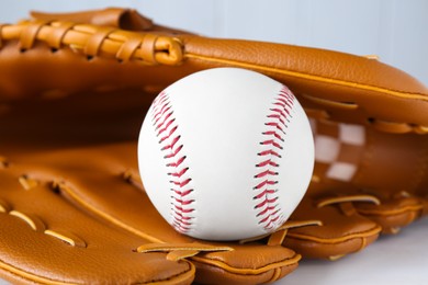 Photo of Leather baseball glove with ball on white wooden table, closeup