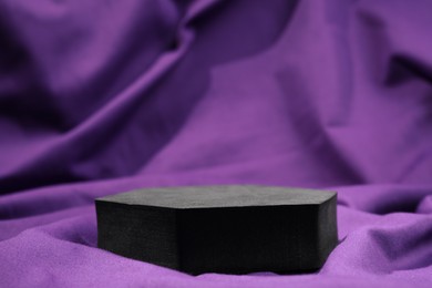 Photo of Black geometric figure on purple fabric, closeup. Stylish presentation for product