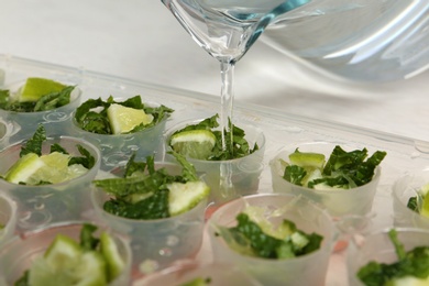 Photo of Pouring water into ice cube tray with lime slices and mint on table, closeup