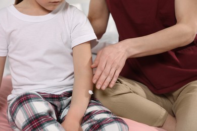 Mother applying ointment onto her daughter's arm on bed, closeup