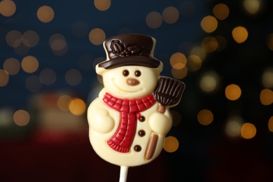 Photo of Funny chocolate snowman candy against blurred festive lights, closeup