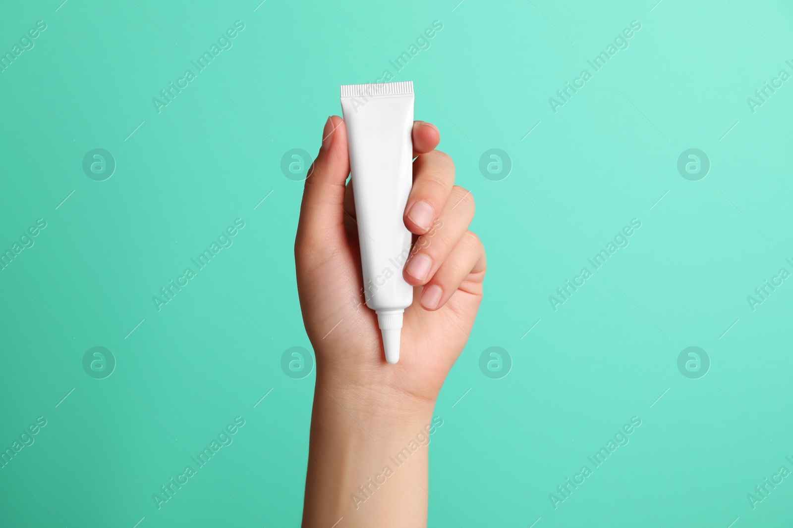 Photo of Woman holding tube of face cream on turquoise background, closeup