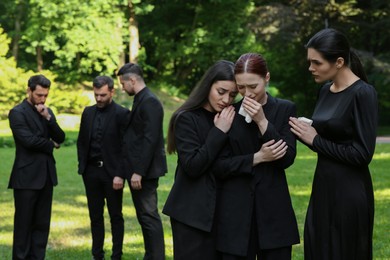 Photo of Sad people in black clothes mourning outdoors. Funeral ceremony