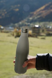 Photo of Boy holding thermo bottle with drink in mountains on sunny day, closeup