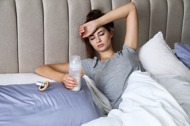 Photo of Exhausted young mother with bottle of milk in bed at home