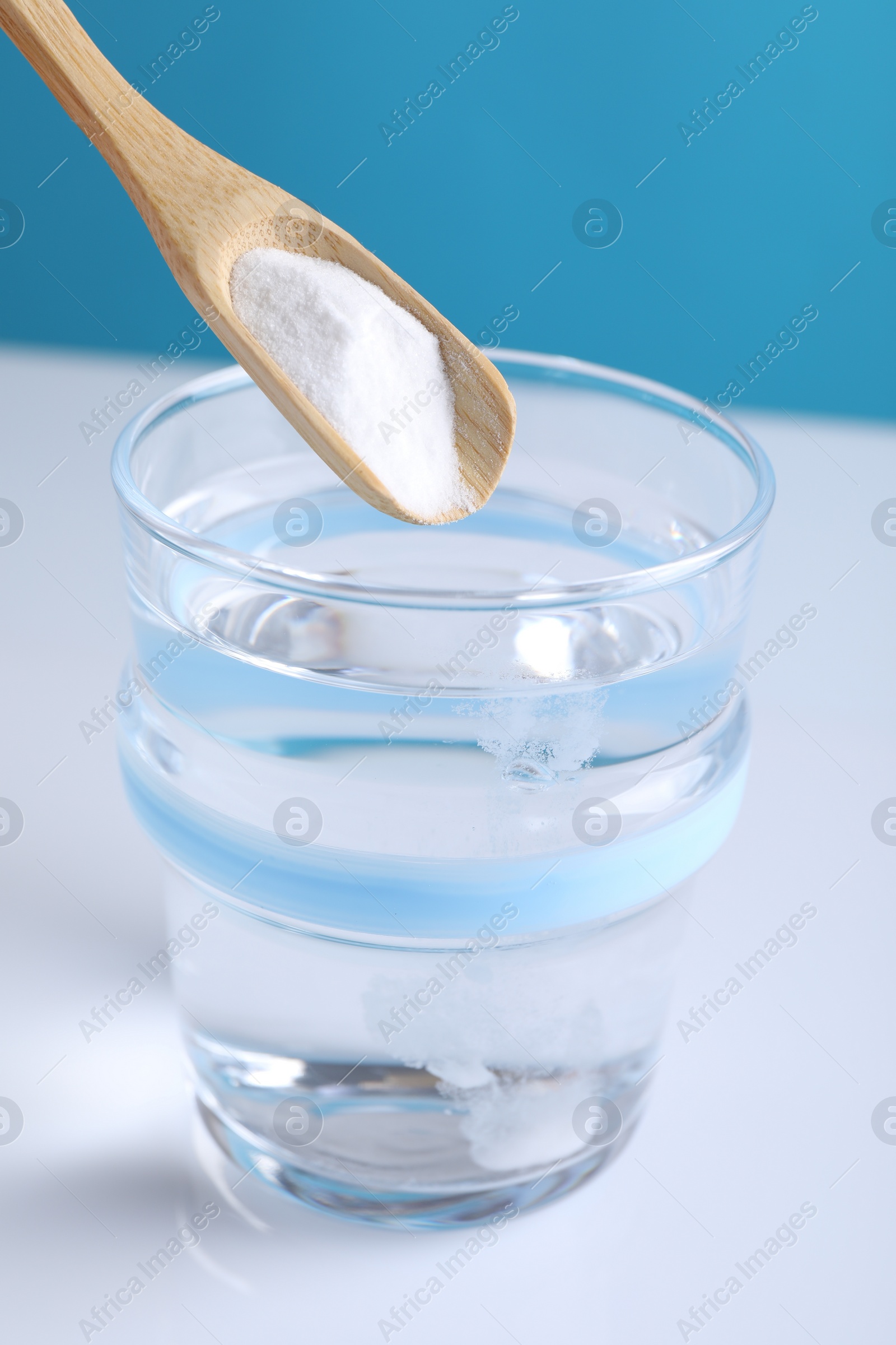 Photo of Adding baking soda into glass of water on color background, closeup