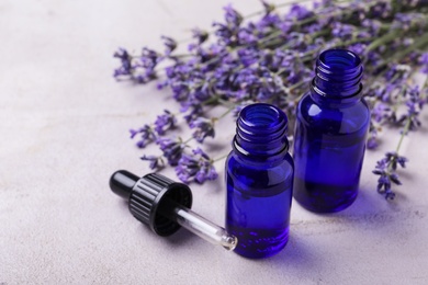 Bottles of essential oil and lavender flowers on stone background