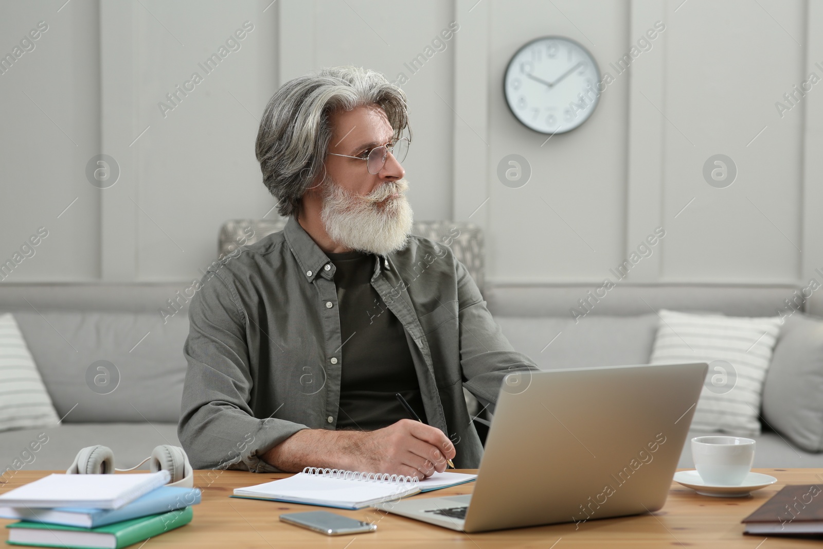 Photo of Middle aged man with laptop and notebook learning at table indoors