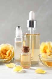 Photo of Bottles and bowl of rose essential oil and fresh flowers on white table