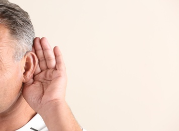 Mature man with hearing problem on light background, closeup. Space for text