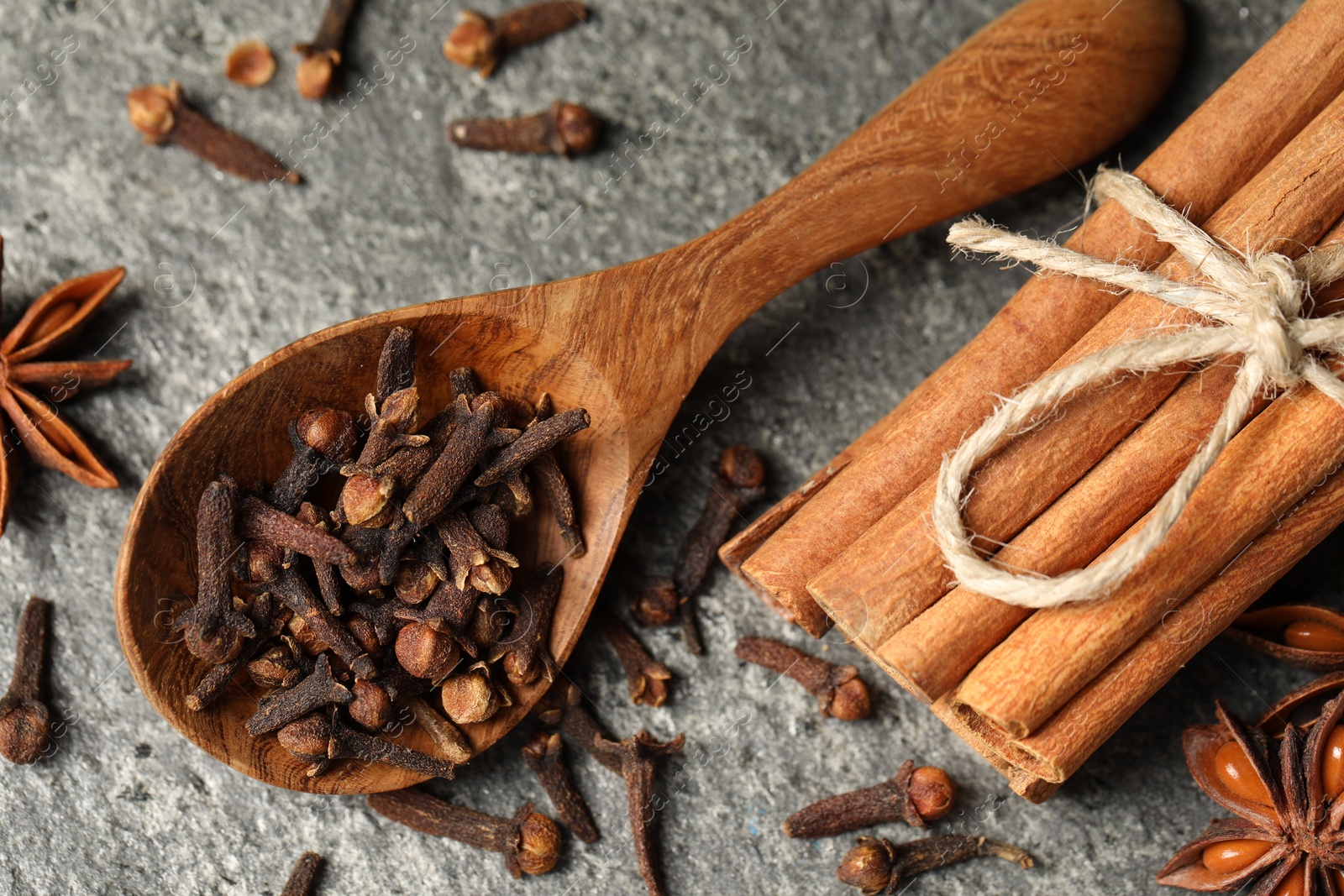 Photo of Wooden spoon with different spices on gray textured table, flat lay