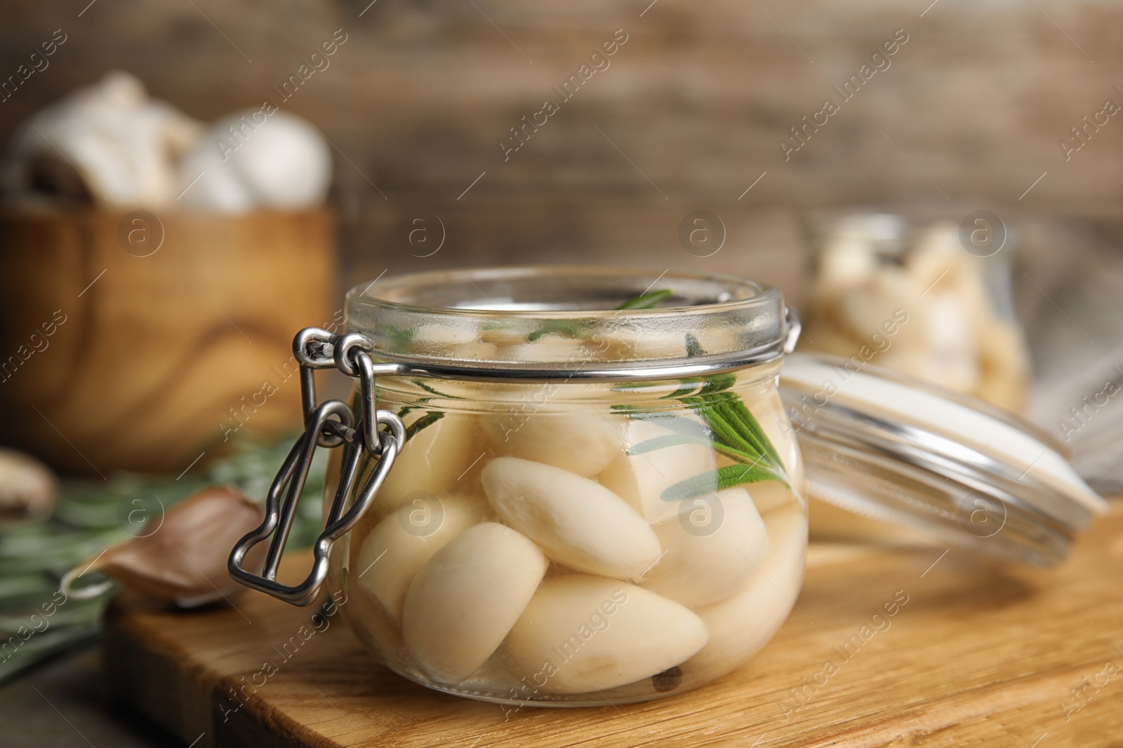 Photo of Composition with jar of pickled garlic on wooden board, closeup