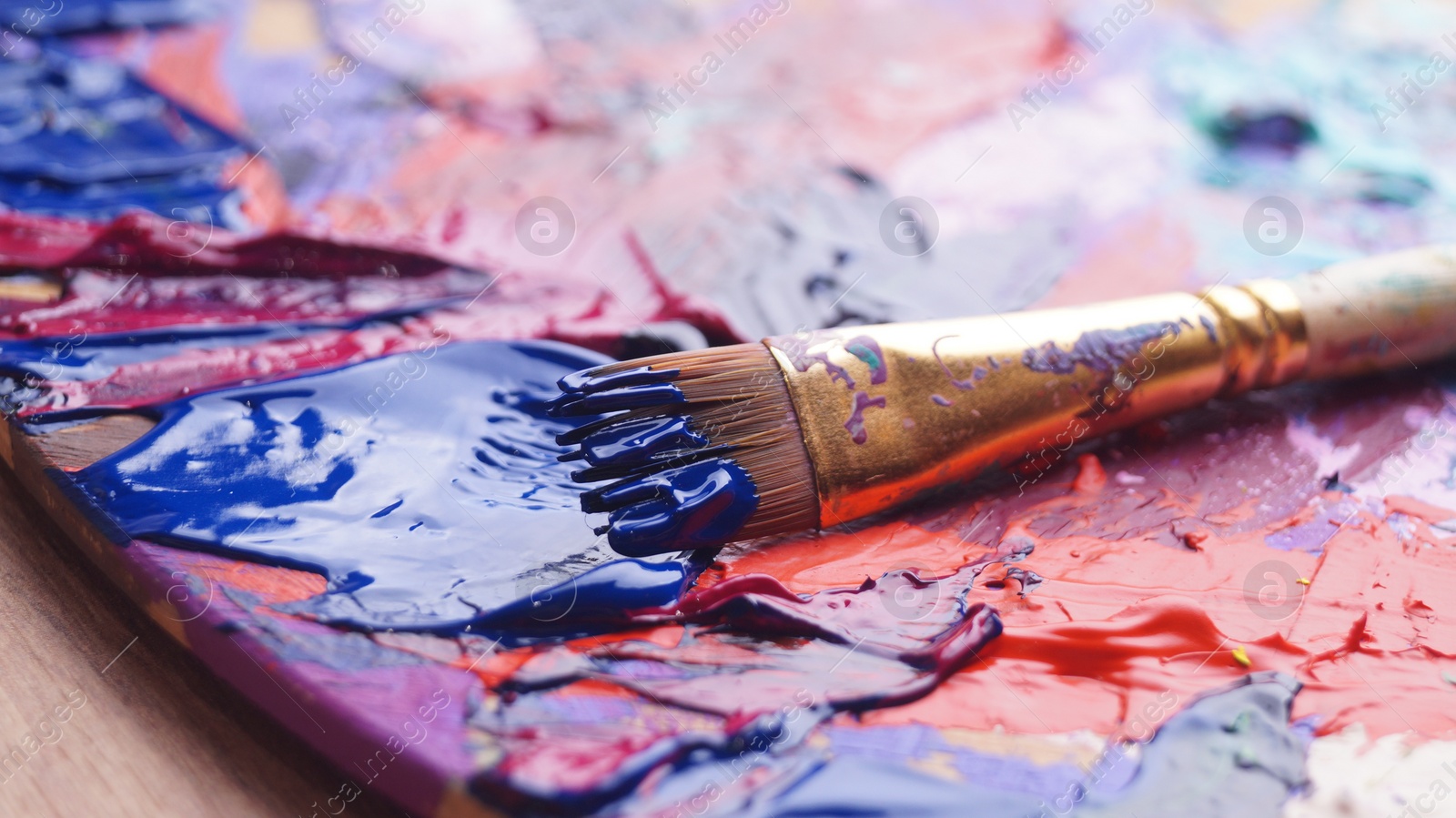 Photo of Brush and artist's palette with mixed paints on wooden table, closeup