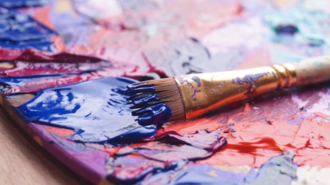 Photo of Brush and artist's palette with mixed paints on wooden table, closeup
