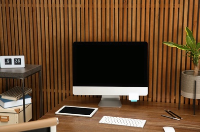 Stylish workplace with modern computer near wooden wall. Space for text