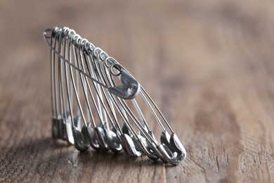 Photo of Many safety pins on wooden table, closeup. Space for text